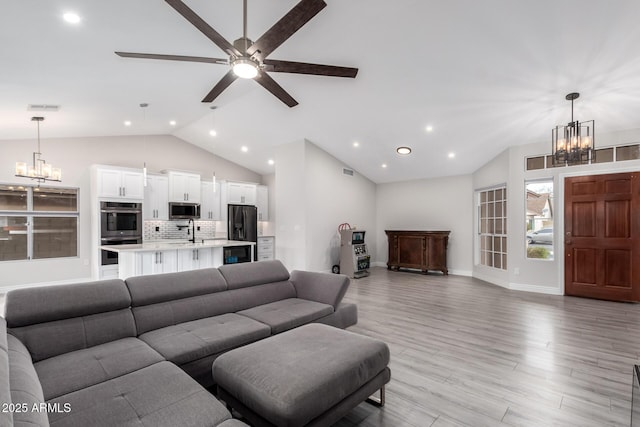 living room with lofted ceiling, light wood-style flooring, ceiling fan with notable chandelier, and visible vents