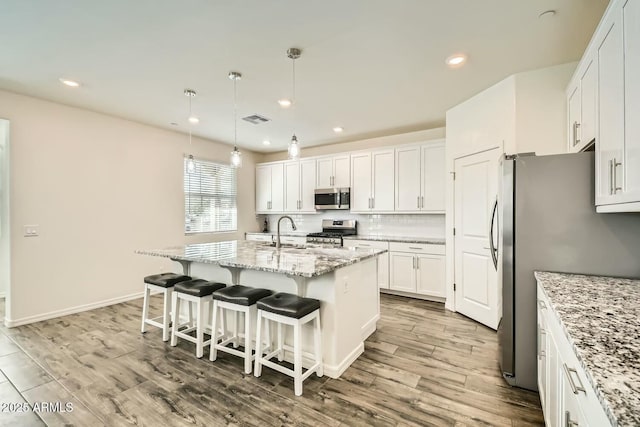 kitchen with decorative light fixtures, a center island with sink, light stone countertops, appliances with stainless steel finishes, and white cabinets