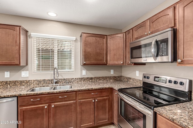 kitchen with light stone counters, brown cabinets, appliances with stainless steel finishes, and a sink