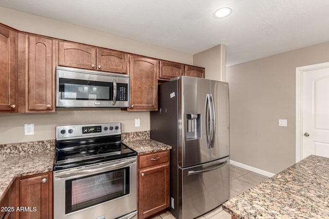 kitchen with light tile patterned floors, light stone countertops, brown cabinets, and stainless steel appliances