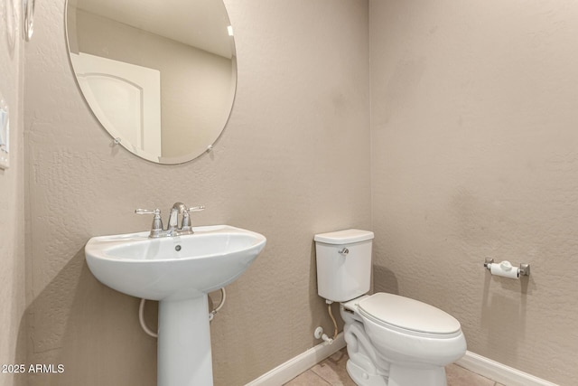 bathroom featuring baseboards, toilet, a textured wall, tile patterned floors, and a sink