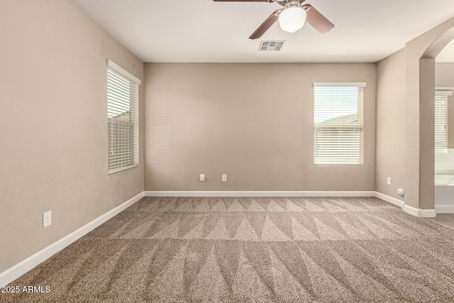 unfurnished room with visible vents, arched walkways, carpet, baseboards, and ceiling fan