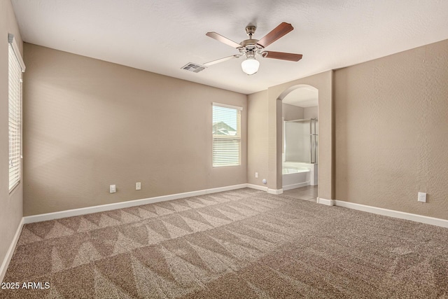 unfurnished bedroom featuring visible vents, light carpet, arched walkways, baseboards, and a textured wall