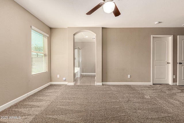 carpeted spare room featuring arched walkways, baseboards, and a textured wall