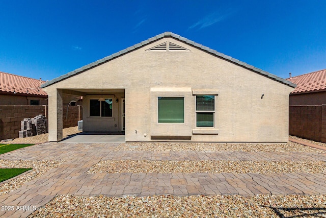 rear view of property with stucco siding, a tiled roof, a patio, and fence