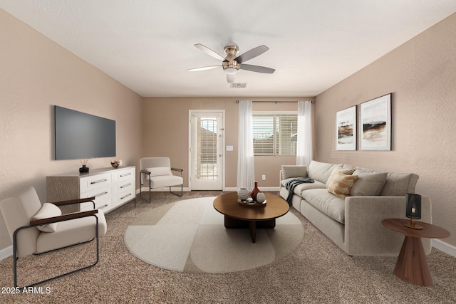 living area featuring visible vents, baseboards, carpet flooring, a textured wall, and a ceiling fan