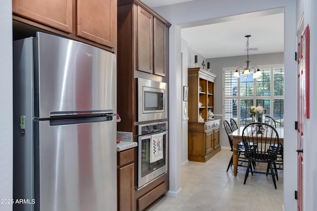 kitchen with pendant lighting, light tile patterned floors, stainless steel appliances, a notable chandelier, and light stone countertops