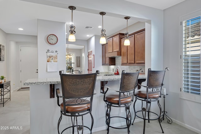 kitchen with pendant lighting, a breakfast bar, light stone counters, decorative backsplash, and kitchen peninsula