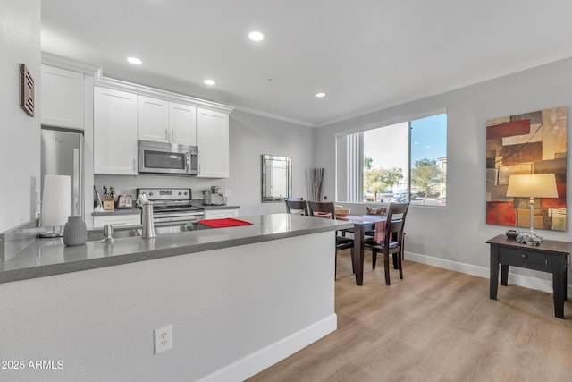 kitchen with white cabinetry, ornamental molding, appliances with stainless steel finishes, kitchen peninsula, and light hardwood / wood-style floors