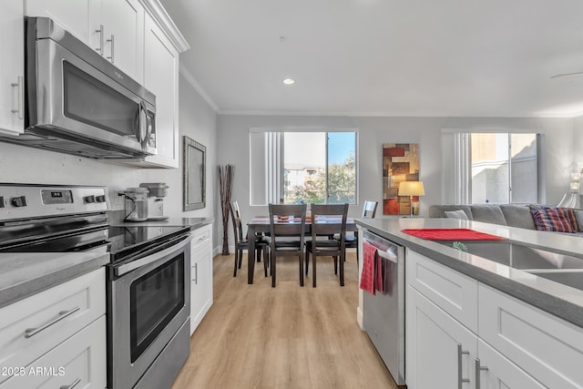 kitchen with stainless steel appliances, ornamental molding, plenty of natural light, and white cabinets