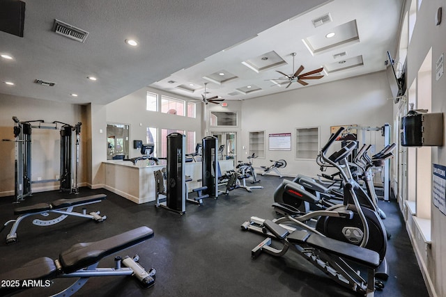 exercise room with coffered ceiling, a textured ceiling, ceiling fan, and a towering ceiling