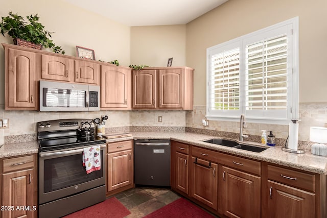 kitchen featuring light stone counters, a sink, appliances with stainless steel finishes, backsplash, and stone finish flooring