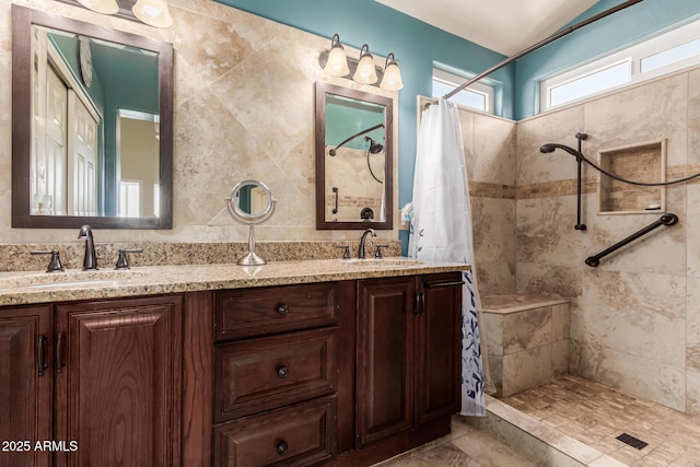 full bath with tiled shower, a sink, and double vanity