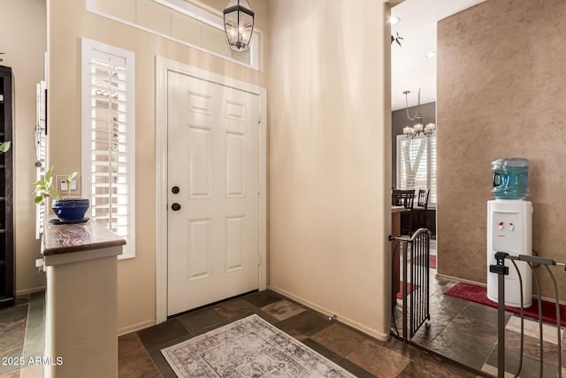 entrance foyer with an inviting chandelier, stone finish flooring, and baseboards