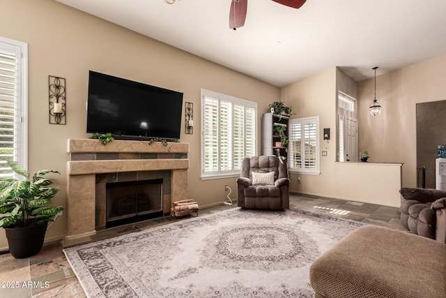 living area featuring ceiling fan, a tile fireplace, and baseboards