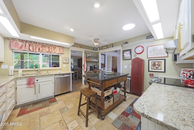 kitchen featuring ceiling fan, dishwasher, a sink, white cabinets, and stone tile floors