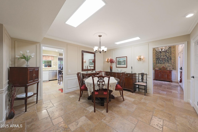 dining space featuring stone tile floors, a chandelier, ornamental molding, and a decorative wall