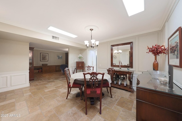 dining space featuring an inviting chandelier, a decorative wall, stone tile flooring, and visible vents