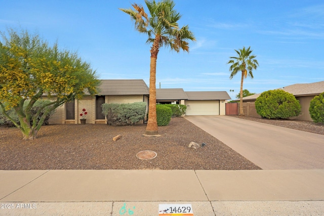 view of front of house featuring an attached garage, fence, brick siding, and concrete driveway