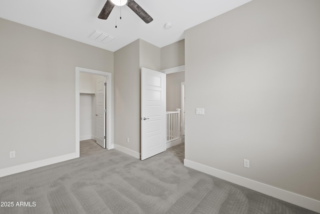 unfurnished bedroom featuring light carpet, a walk in closet, a closet, and ceiling fan