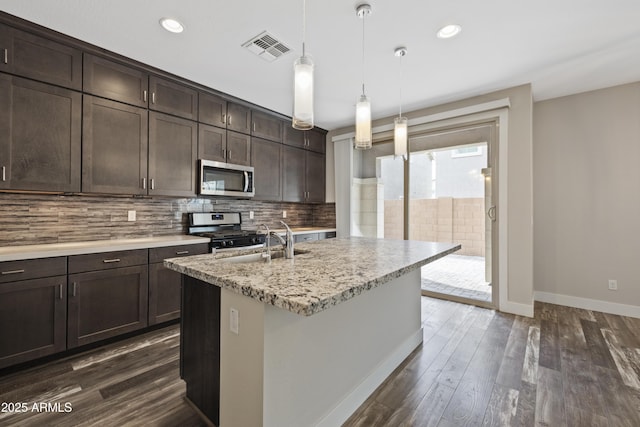 kitchen featuring appliances with stainless steel finishes, pendant lighting, sink, a kitchen island with sink, and dark brown cabinetry