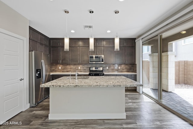 kitchen featuring hanging light fixtures, stainless steel appliances, light stone countertops, and a center island with sink