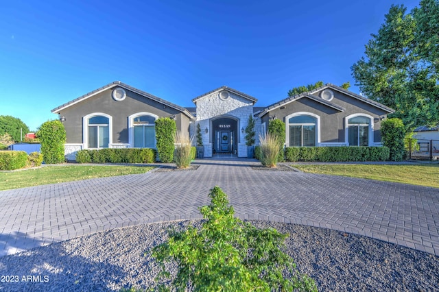 view of front of home with stone siding, stucco siding, decorative driveway, and a front yard