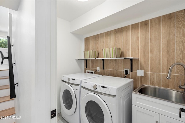 clothes washing area with separate washer and dryer, sink, and cabinets