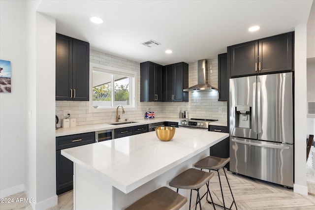 kitchen with sink, stainless steel appliances, a center island, a kitchen bar, and wall chimney exhaust hood