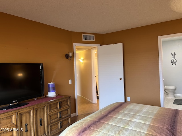 bedroom with light tile patterned flooring, ensuite bath, and a textured ceiling