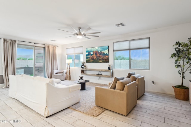 living room featuring a wealth of natural light, visible vents, wood finish floors, and a ceiling fan