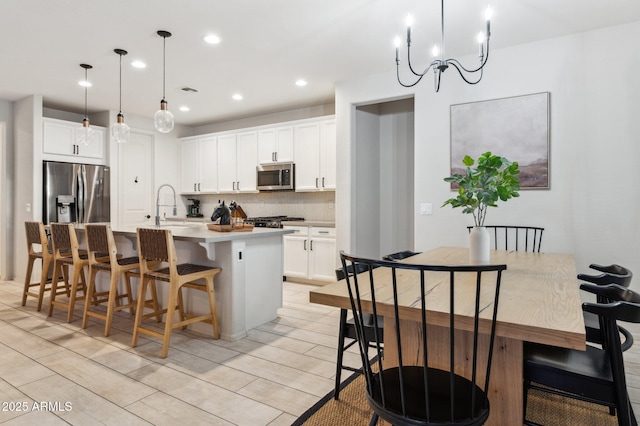 kitchen with an island with sink, a kitchen breakfast bar, tasteful backsplash, white cabinetry, and appliances with stainless steel finishes