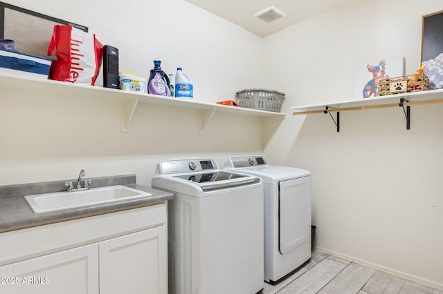 laundry area featuring visible vents, a sink, light wood-style flooring, cabinet space, and separate washer and dryer