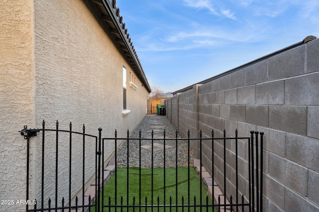 view of property exterior with a yard, stucco siding, a fenced backyard, and a gate