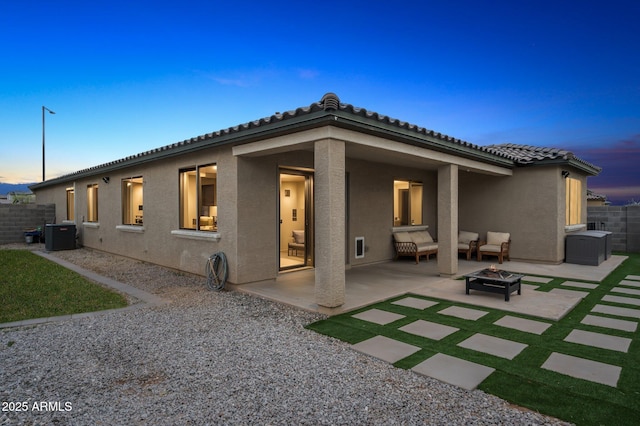 back of property at dusk featuring stucco siding, a tile roof, a patio, fence, and an outdoor fire pit