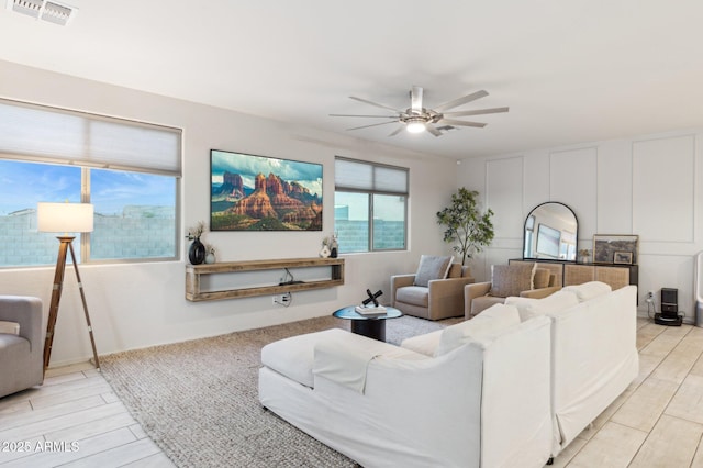 living area with visible vents, a decorative wall, a ceiling fan, and wood tiled floor