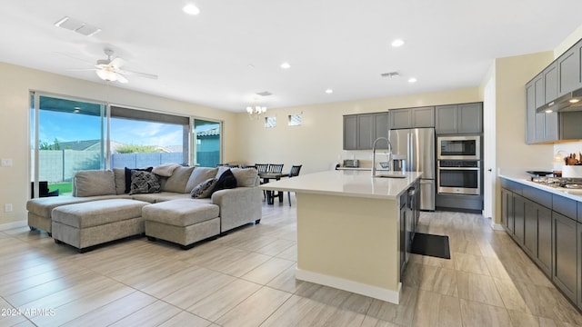 kitchen with a kitchen breakfast bar, gray cabinets, an island with sink, and appliances with stainless steel finishes