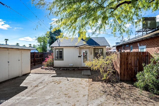 back of house with central AC unit and a storage unit