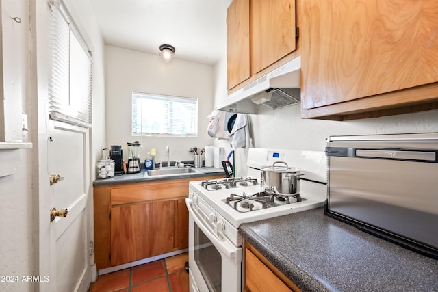 kitchen featuring white gas range oven, dark tile patterned floors, and sink