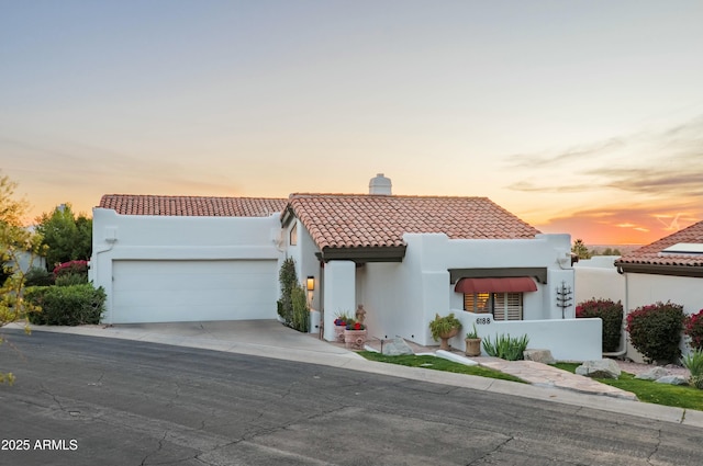 mediterranean / spanish home with a garage, a tiled roof, driveway, stucco siding, and a chimney