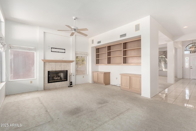 unfurnished living room featuring ceiling fan, a tile fireplace, and light carpet