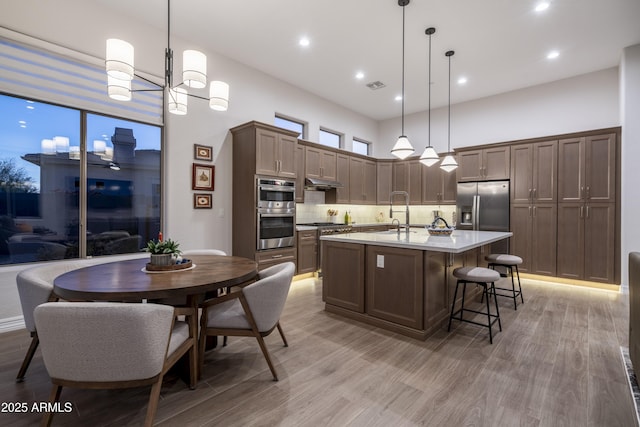 kitchen featuring appliances with stainless steel finishes, pendant lighting, sink, decorative backsplash, and a kitchen island with sink