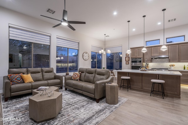 living room featuring ceiling fan with notable chandelier and light wood-type flooring