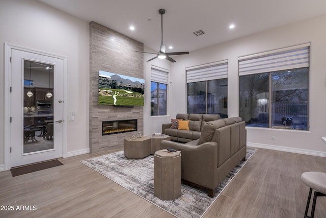 living room featuring ceiling fan, a tiled fireplace, and light hardwood / wood-style floors