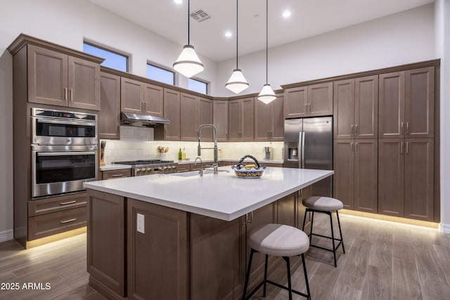 kitchen with sink, hanging light fixtures, a kitchen breakfast bar, stainless steel appliances, and a kitchen island with sink