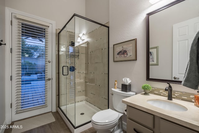 bathroom featuring vanity, toilet, a shower with door, and backsplash