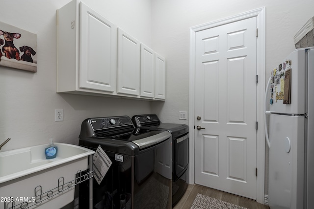 clothes washing area with cabinets, wood-type flooring, and washer and dryer