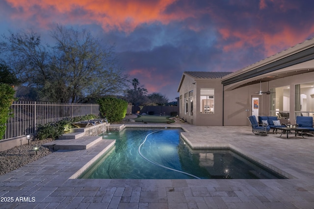 pool at dusk featuring pool water feature, ceiling fan, and a patio