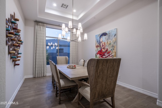 dining area with dark hardwood / wood-style flooring, a raised ceiling, and an inviting chandelier