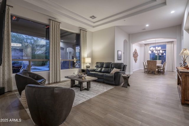 living room featuring a tray ceiling, a chandelier, and light wood-type flooring